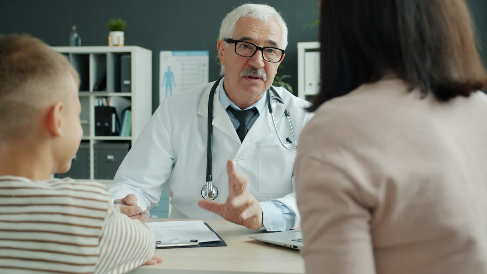 Médico conversando con una madre y su hijo en el consultorio